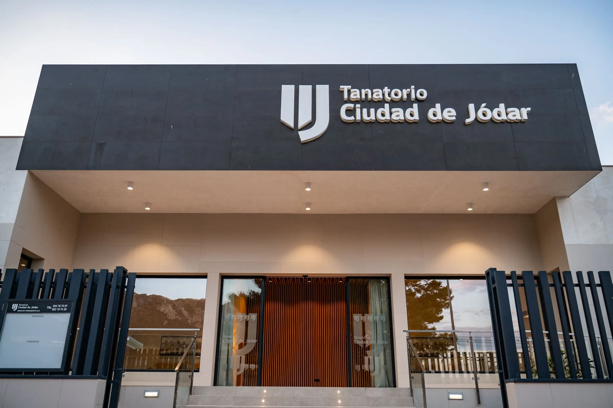 Fachada del tanatorio al atardecer, con el rótulo iluminado