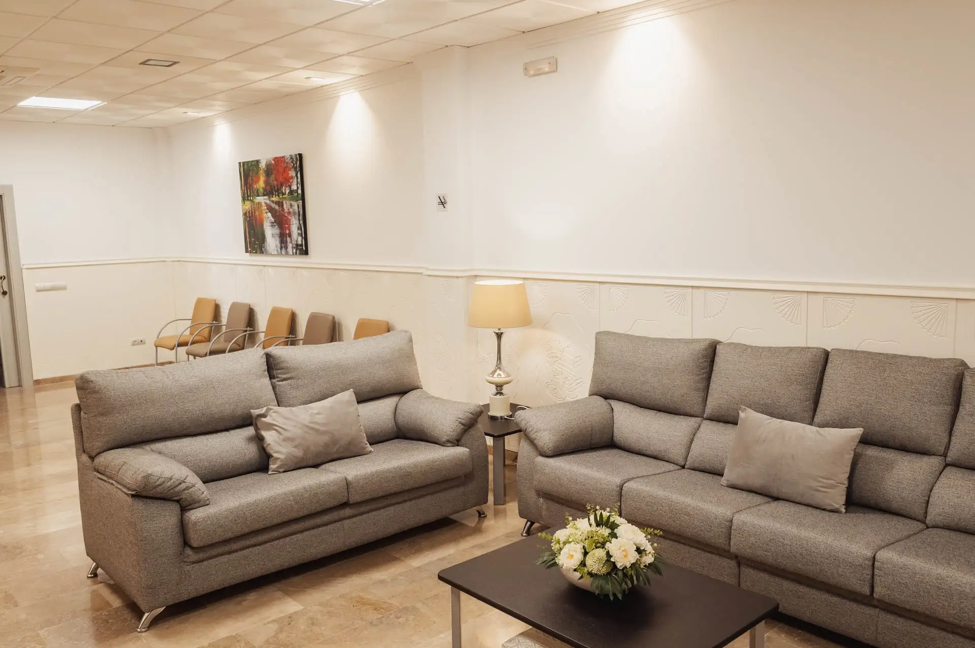 Dos sofás grises con cojines y una mesa con un centro de flores blancas