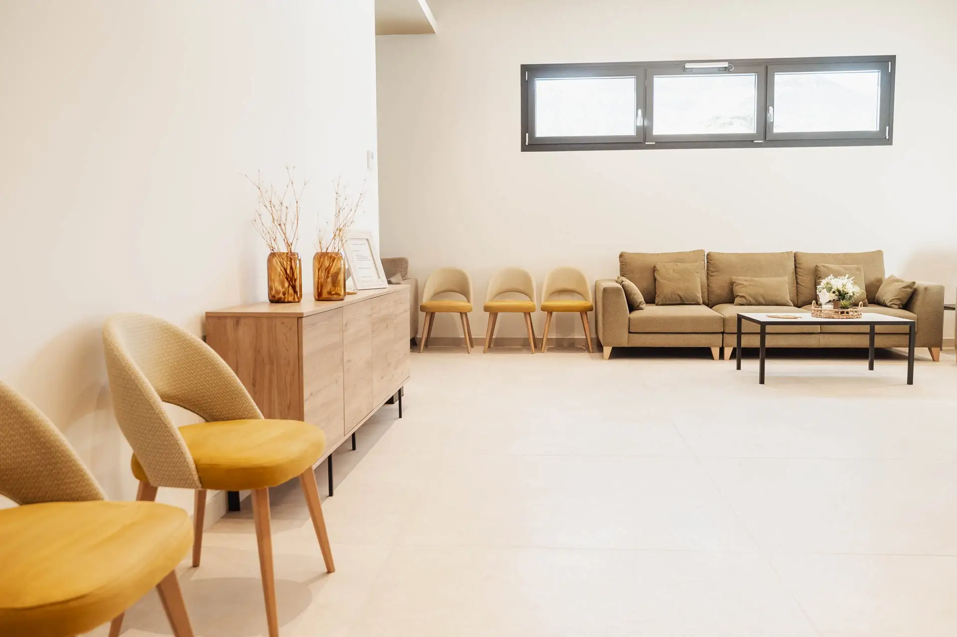 Butacas tapizadas en mostaza, mueble de madera con jarrones y sofá al fondo