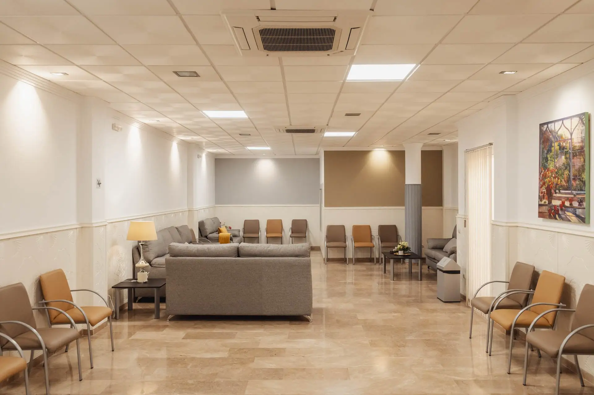Sala de velatorio amplia con sofás grises, sillas y suelo de mármol